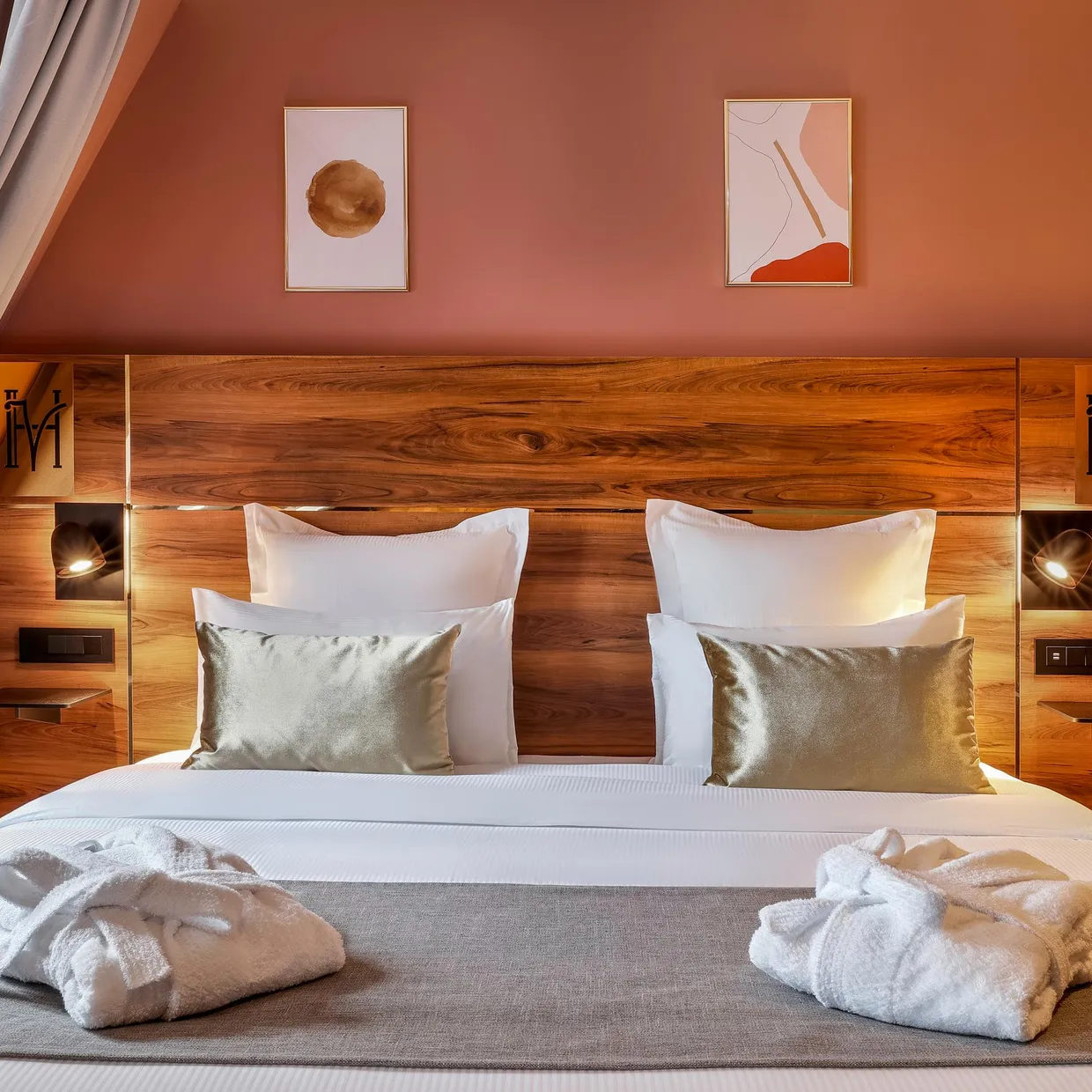 Lit double avec une tête de lit en bois, des oreillers blancs et des serviettes pliées sur la couverture grise