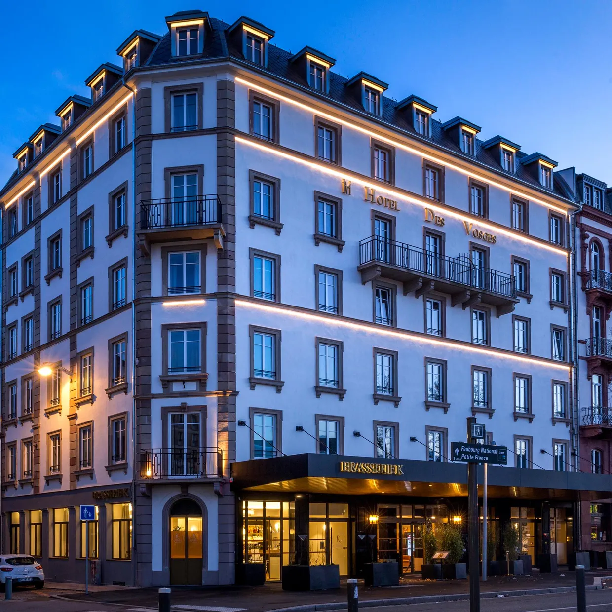 Immeuble d'angle éclairé de nuit avec l'enseigne "Hotel Des Voyageurs" et un restaurant au rez-de-chaussée