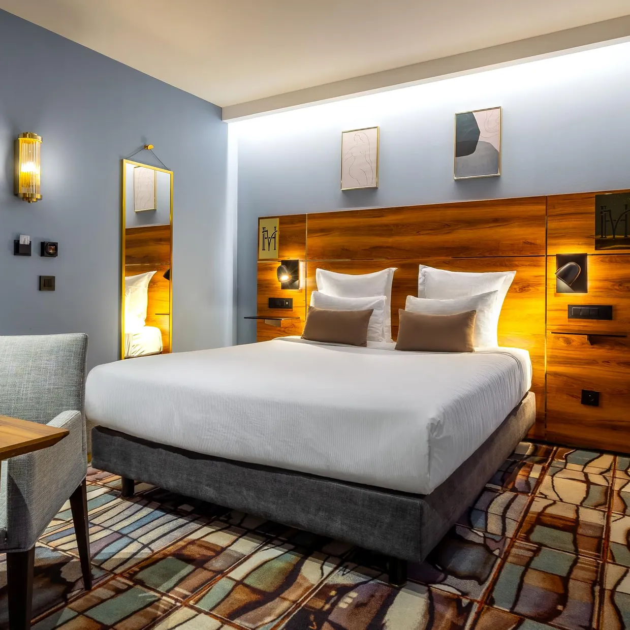 Chambre d'hôtel avec un lit double, une table de travail avec un ordinateur portable, un fauteuil et des œuvres d'art sur les murs