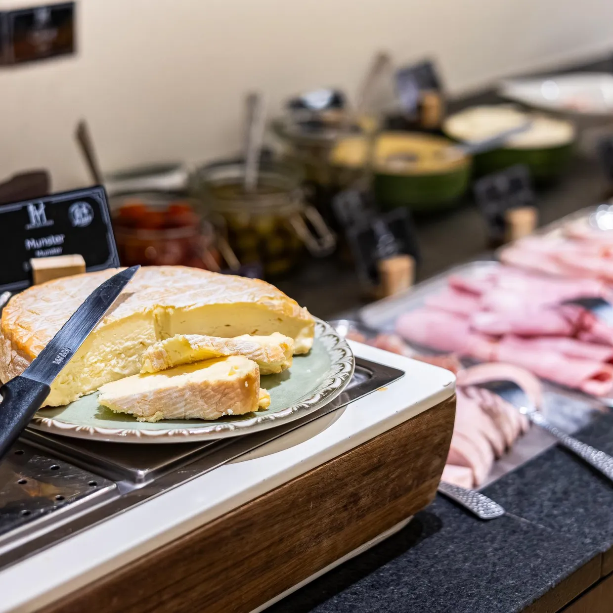 Un plateau de fromage avec un couteau, des morceaux de fromage à pâte dure et des charcuteries sur une table de buffet