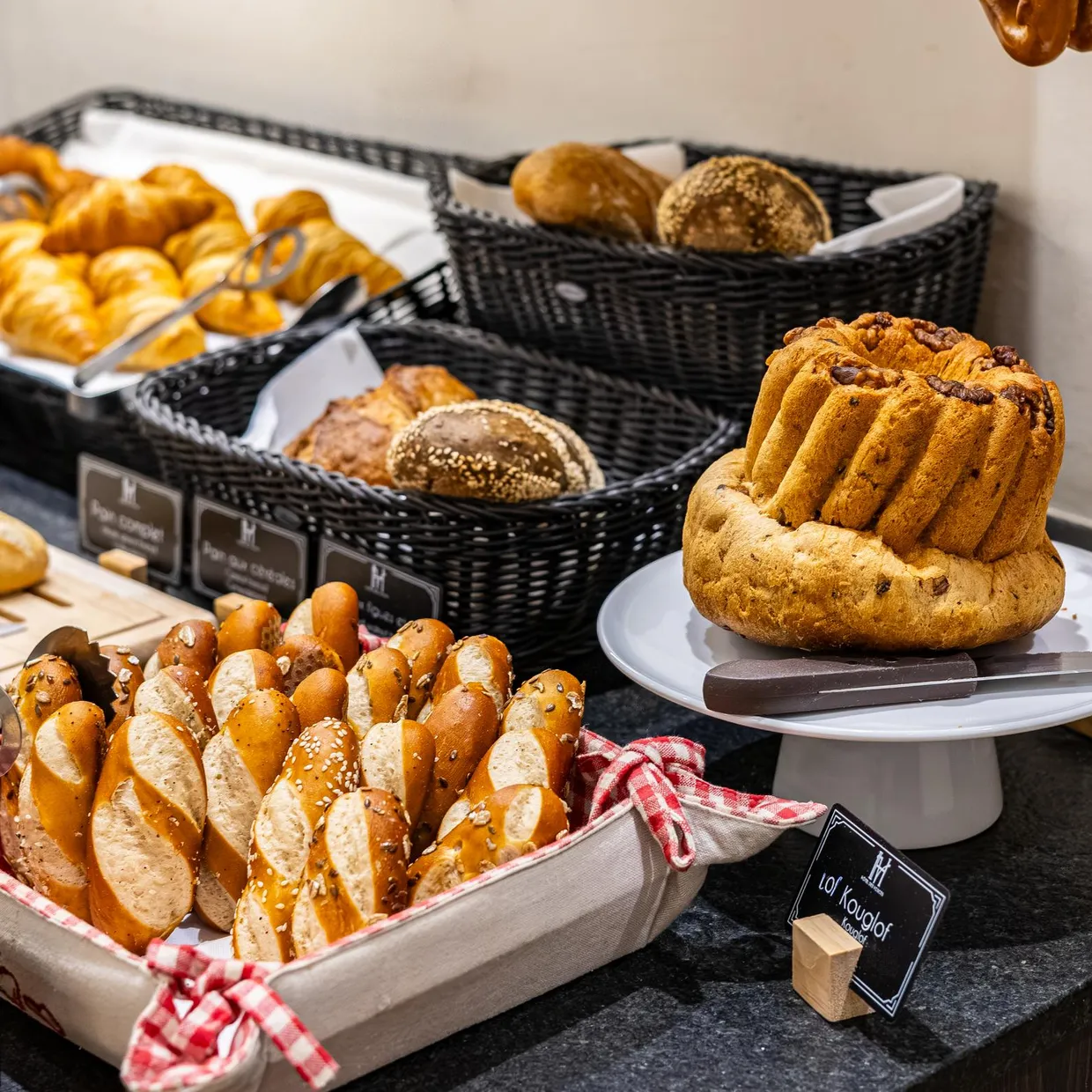 Assortiment de pains et viennoiseries présentés sur des plateaux et dans des paniers en osier avec des étiquettes