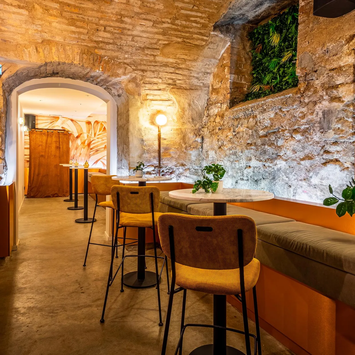 Un intérieur de café avec des murs en briques apparentes, des tables rondes, des chaises et des plantes décoratives