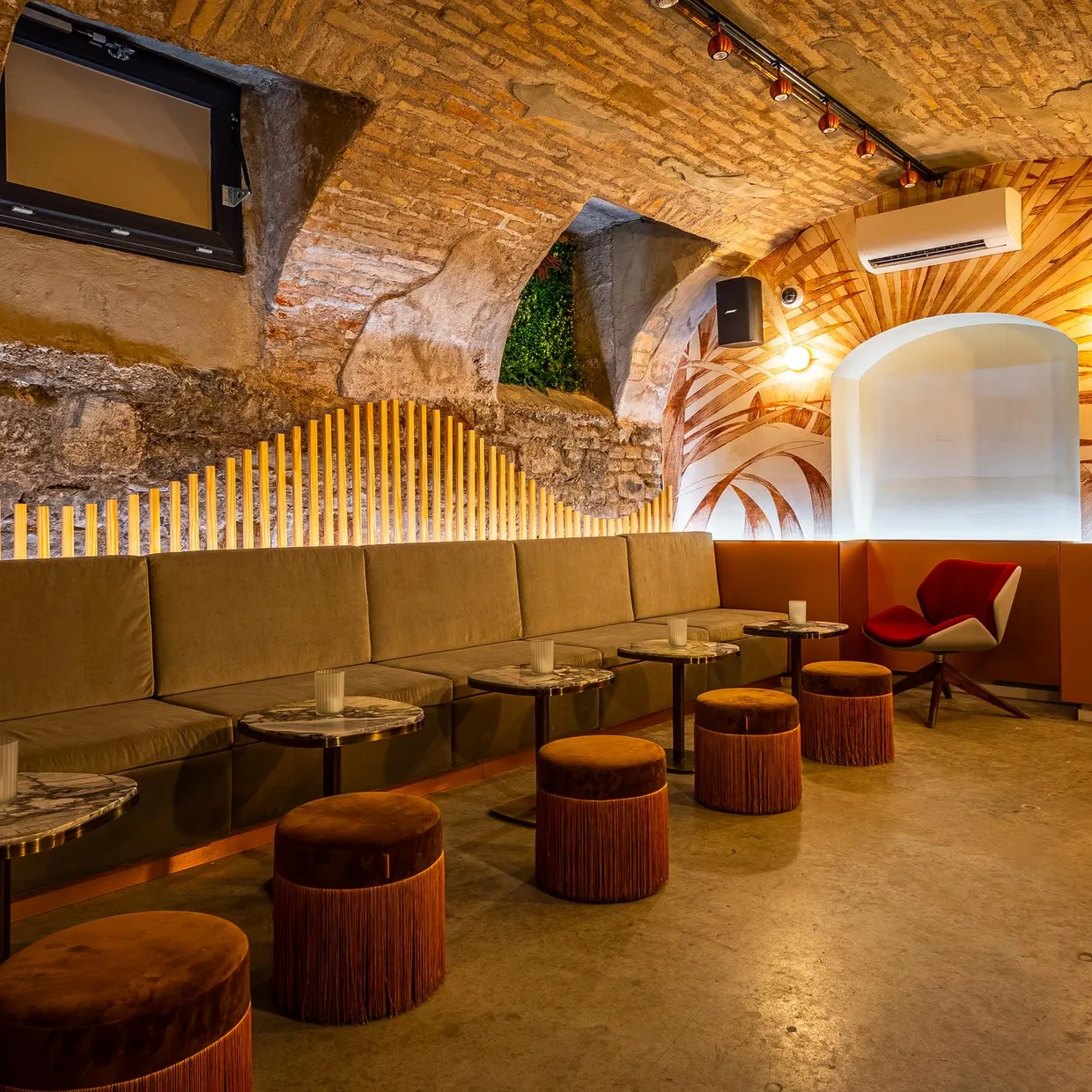 Un intérieur de bar ou café aménagé dans une cave voûtée en pierre avec des sièges en cuir, des tables basses et des tabourets en bois