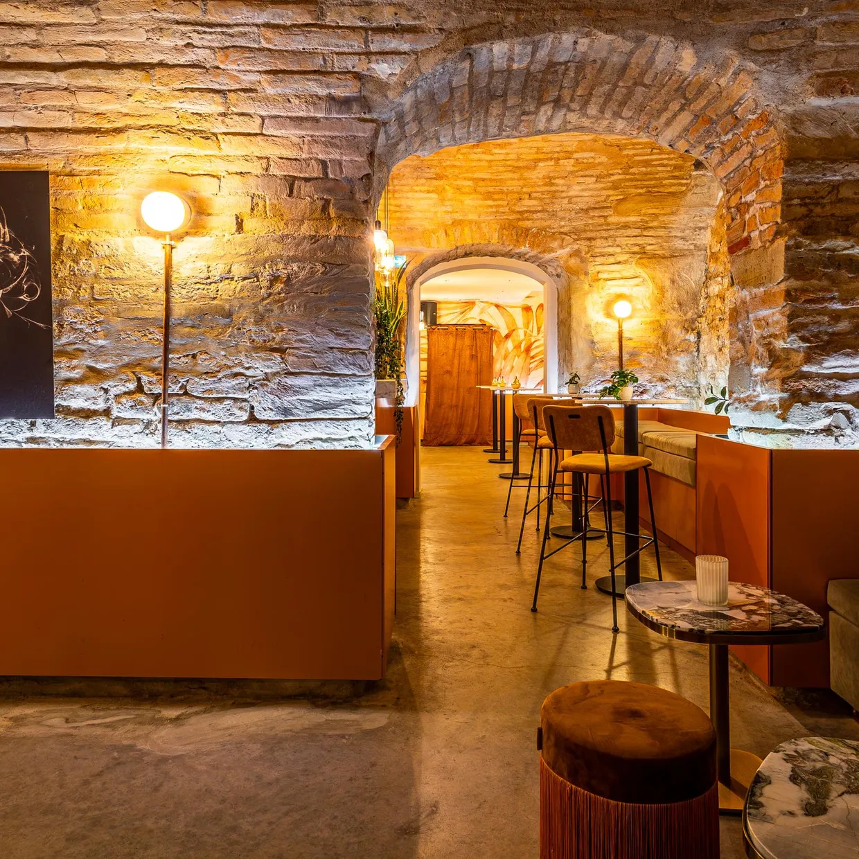 Un intérieur de bar ou restaurant avec des murs en pierre apparente, des lampes sur pied, des tables et des banquettes, éclairé par une lumière chaude