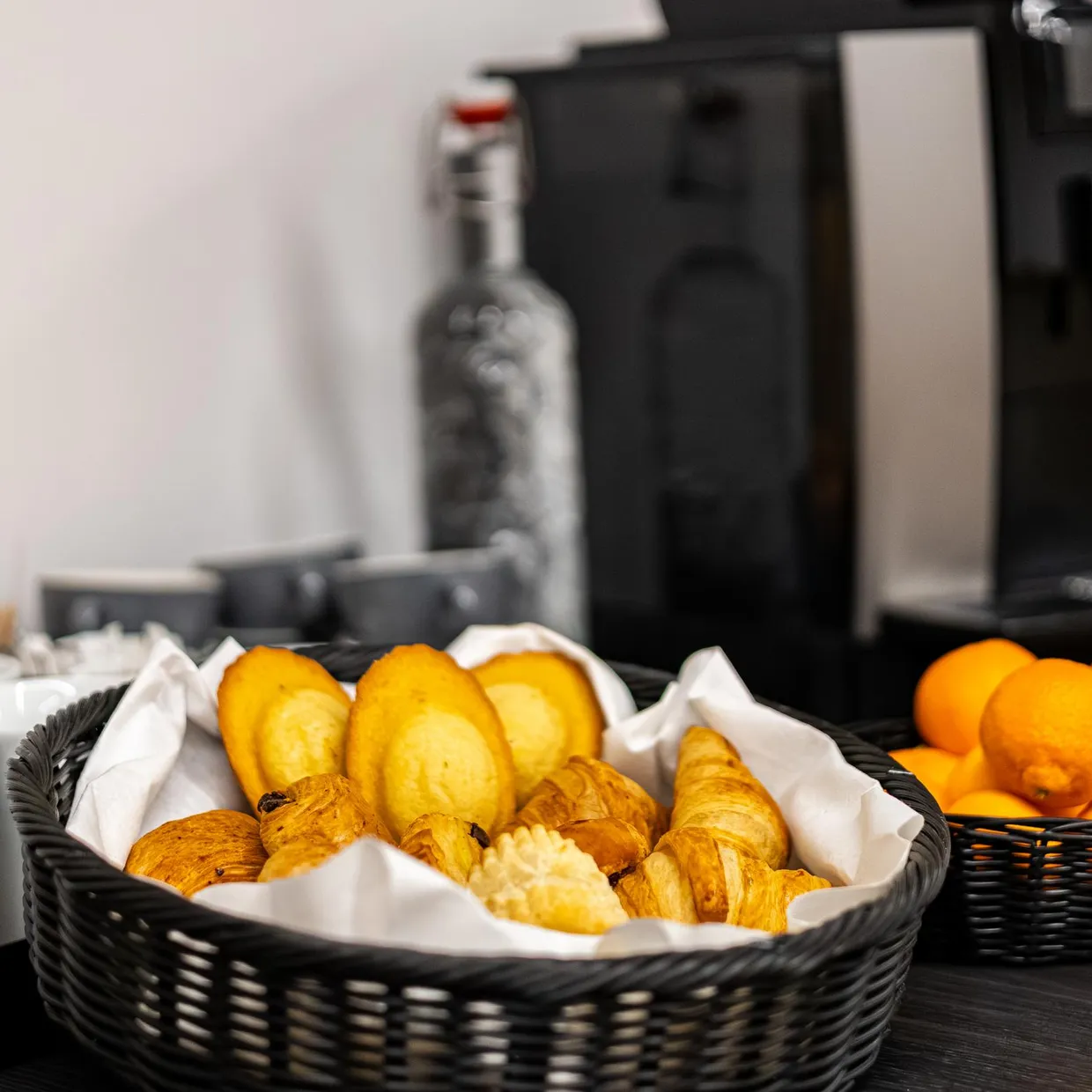 Un plateau avec des croissants, des oranges et des tasses à café devant une machine à café