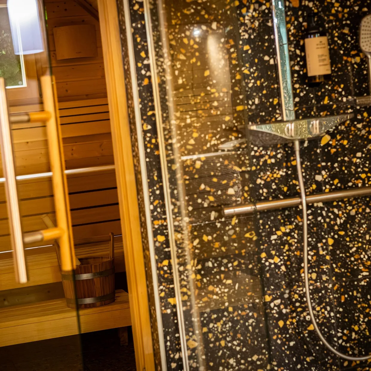 Salle en bois avec parois vitrées et équipements de douche, incluant un pommeau de douche et une paroi en verre dépoli