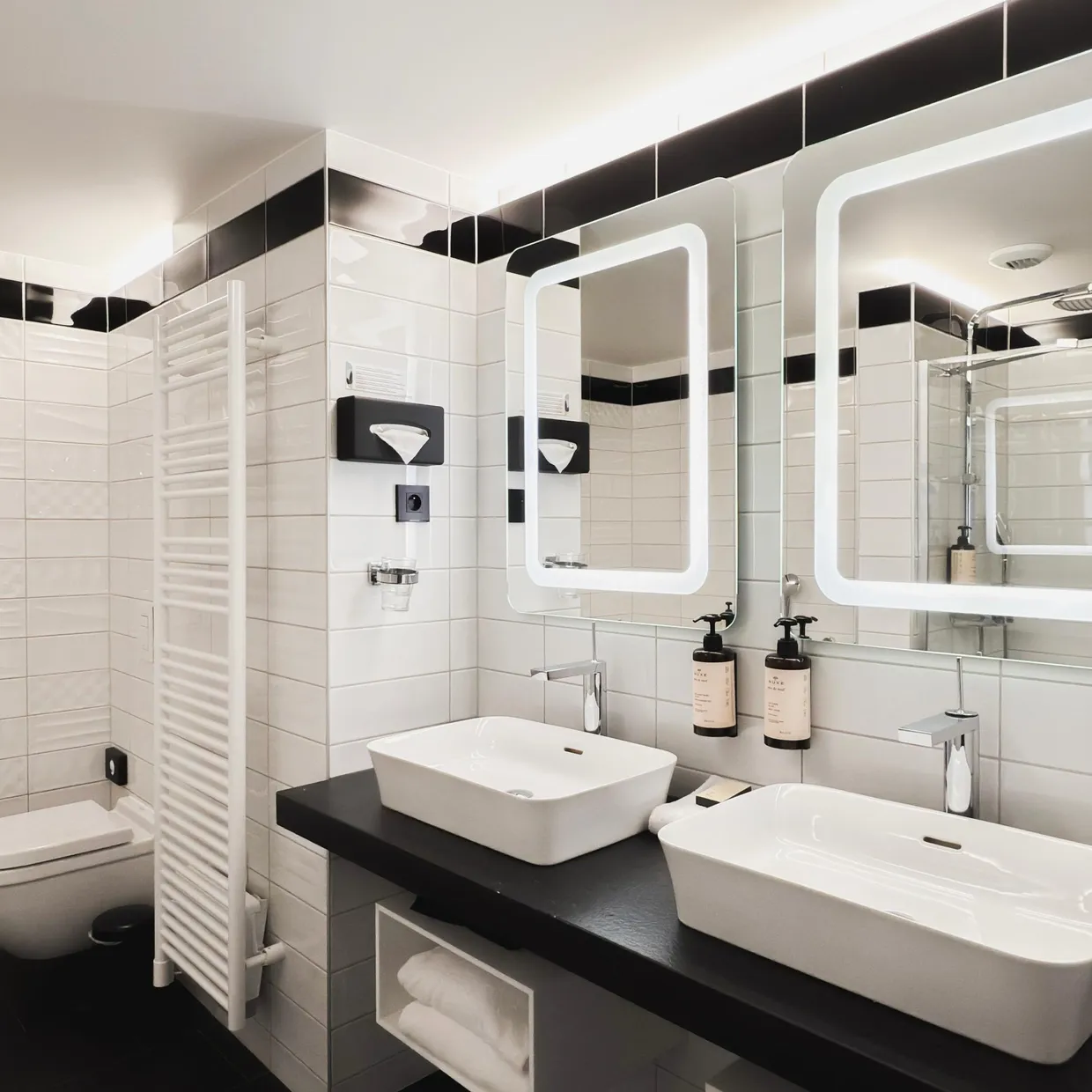 Salle de bain moderne avec toilettes, lavabo, baignoire, miroirs éclairés et serviettes suspendues