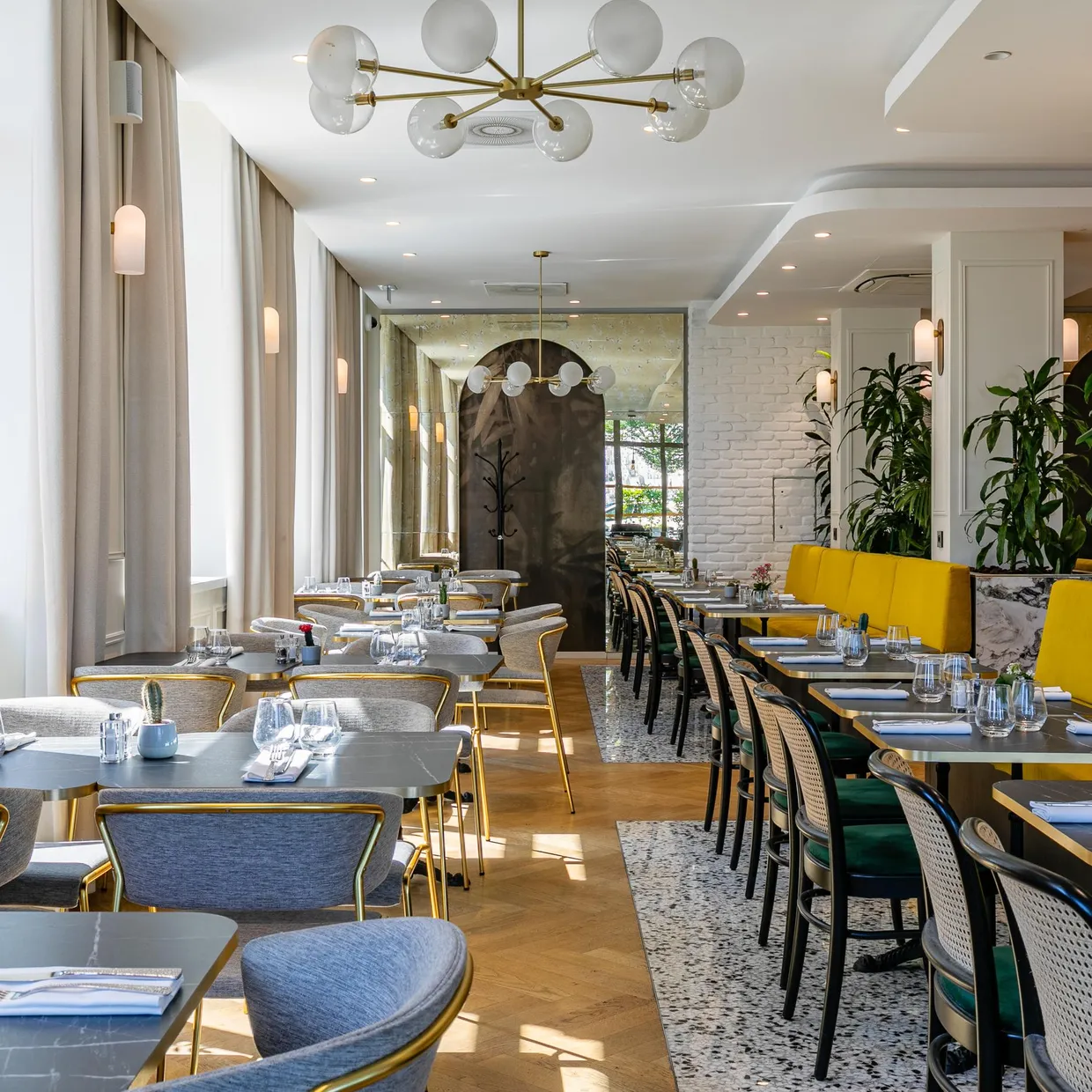 Restaurant moderne avec des tables et des chaises disposées le long d'un couloir, des plantes vertes et des luminaires suspendus