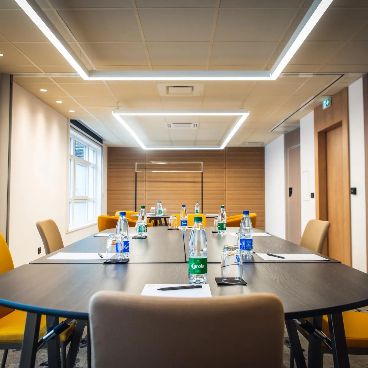 Salle de réunion avec une table rectangulaire, des chaises jaunes et des bouteilles d'eau sur la table