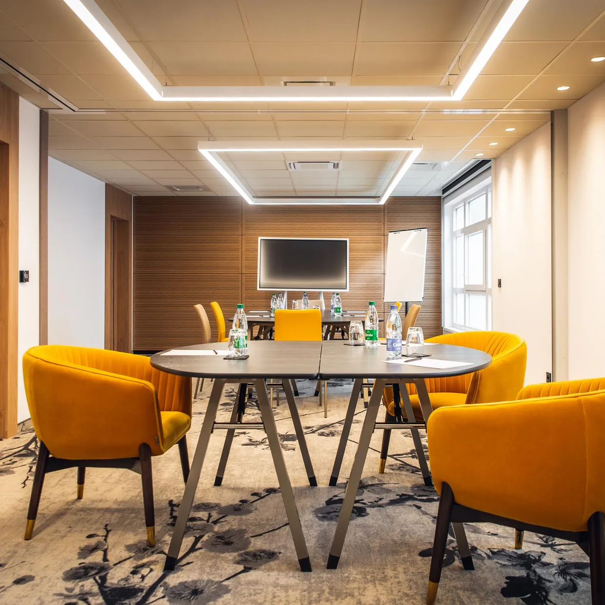 Salle de réunion avec table ronde, chaises jaunes et écran au fond