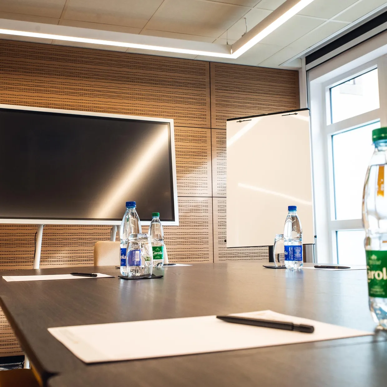 Salle de réunion avec une table, des bouteilles d'eau et un écran allumé sur un mur