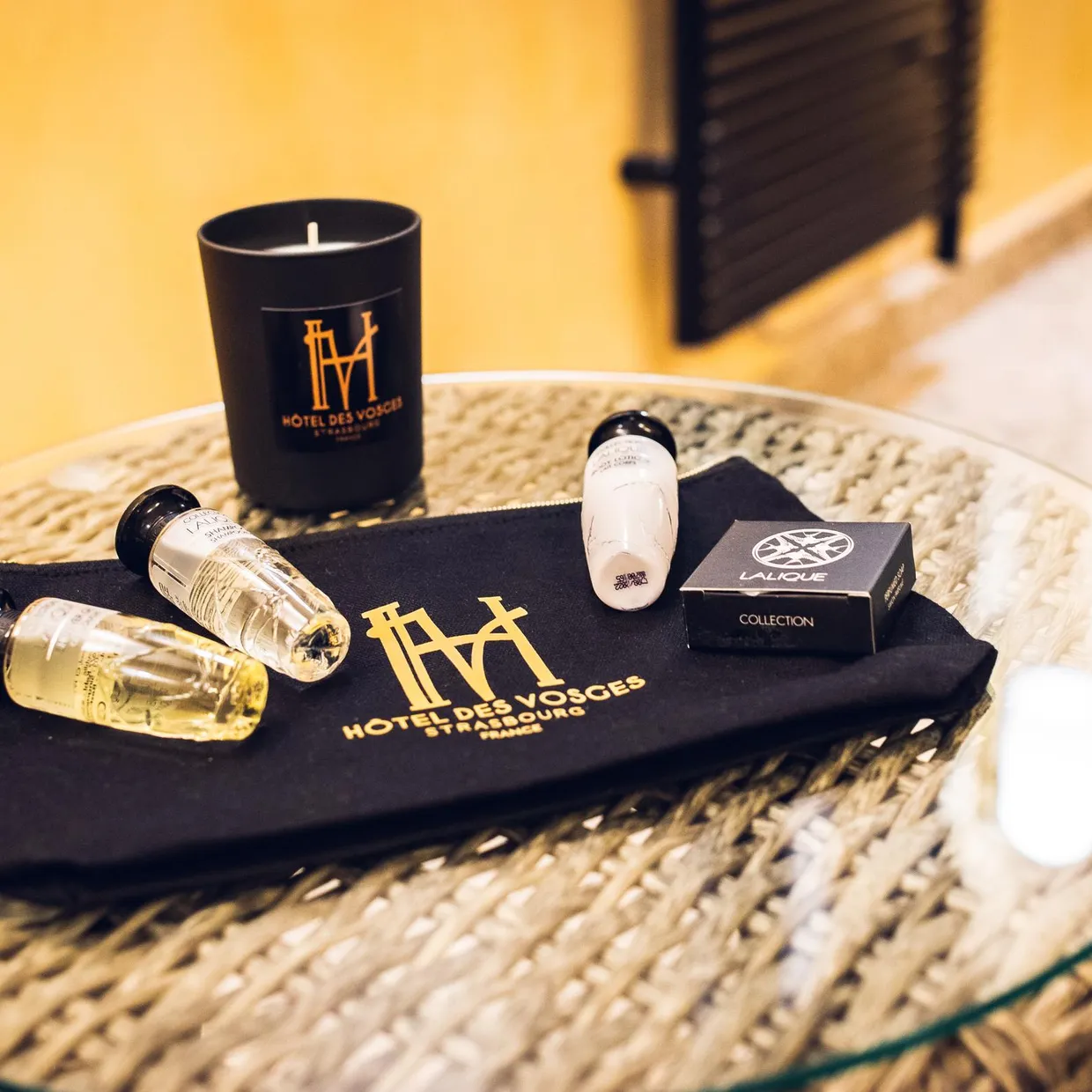 Un plateau avec des flacons de produits cosmétiques, une bougie et un petit coffret sur une table en rotin