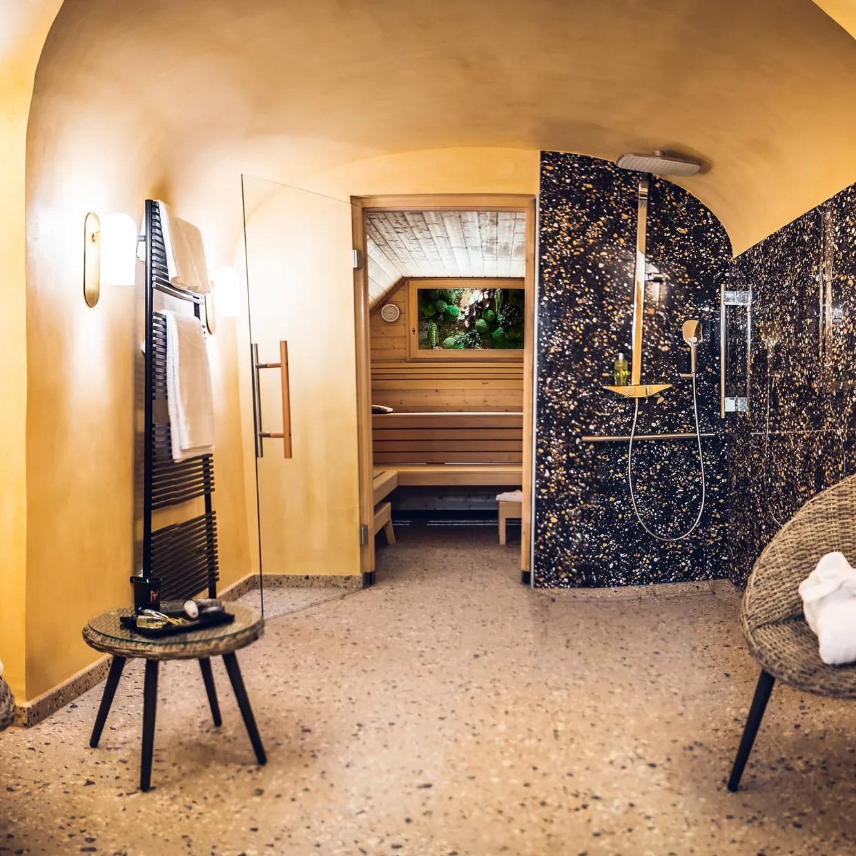 Salle de spa avec deux chaises en osier, des serviettes, une douche et une entrée vers un sauna en bois