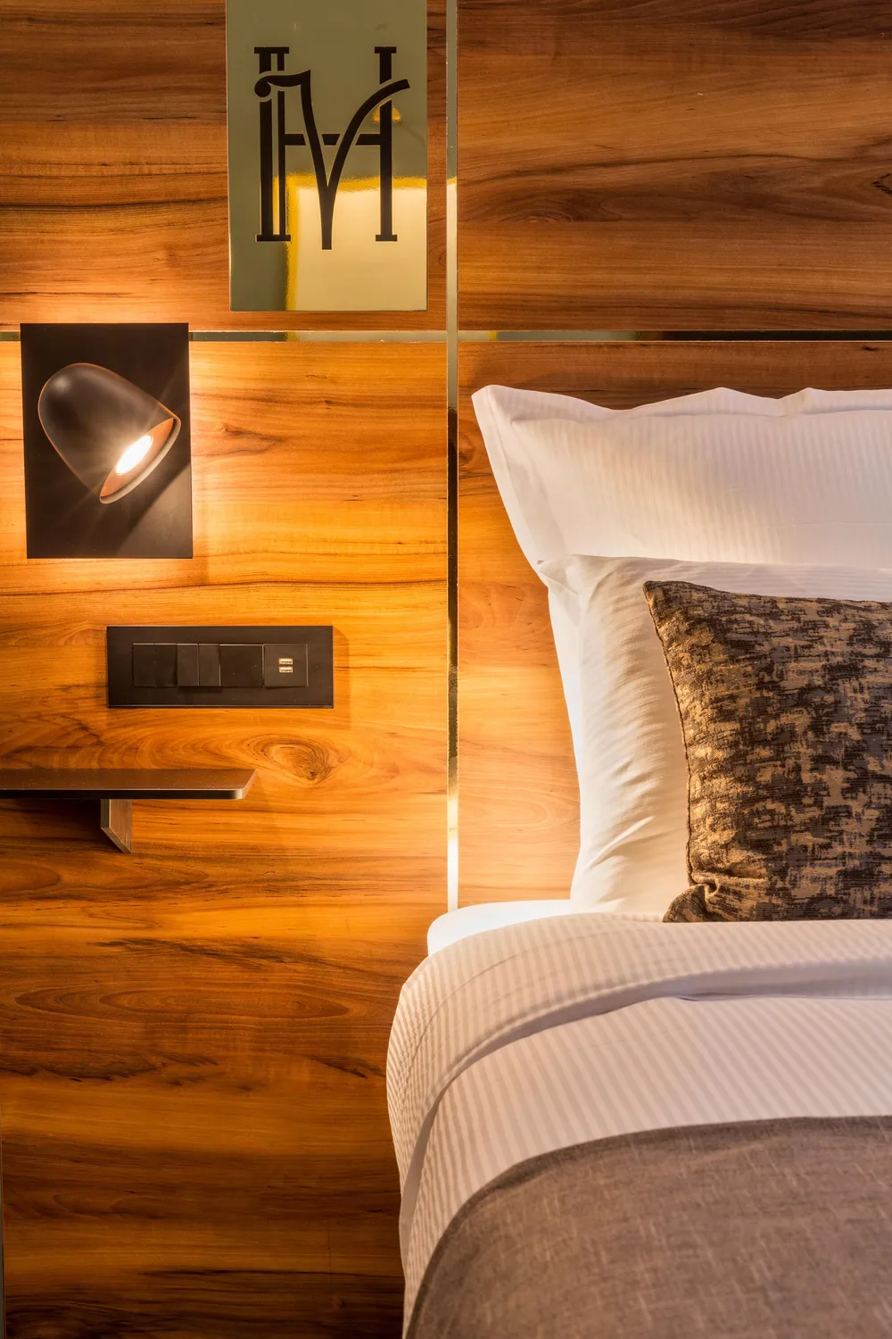 Lit avec une tête de lit en bois, une lampe murale allumée et des oreillers blancs et gris