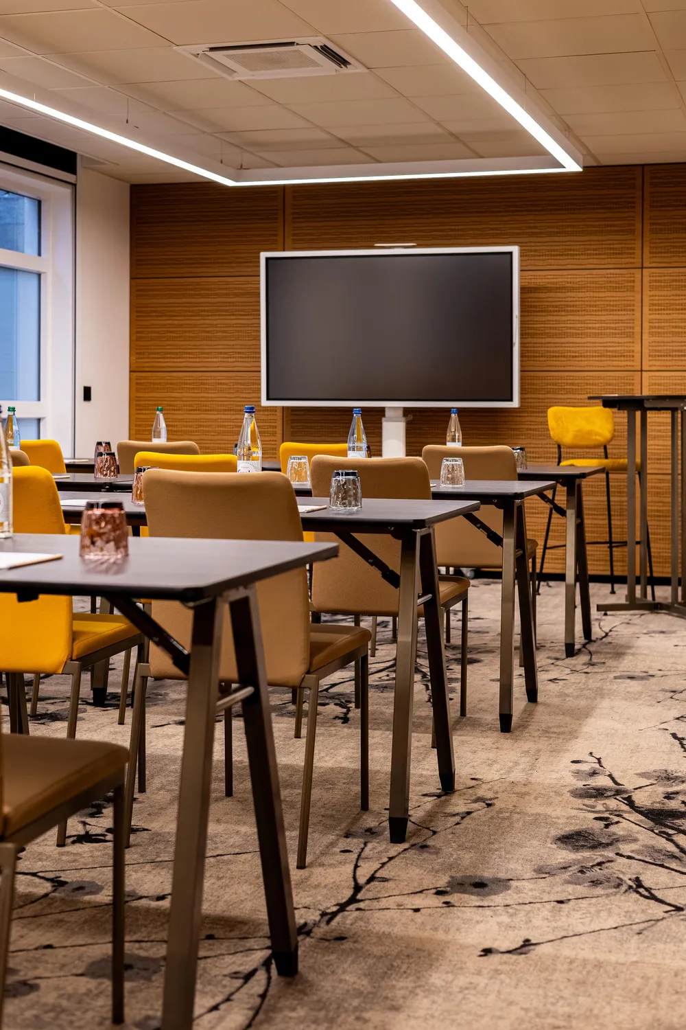 Salle de réunion avec tables, chaises, bouteilles d'eau et écran éteint au fond