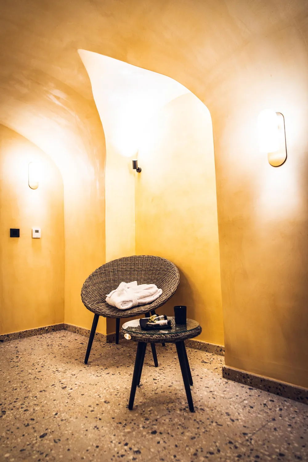 Chaise en rotin avec serviette et table basse dans une pièce aux murs jaunes et au sol granuleux