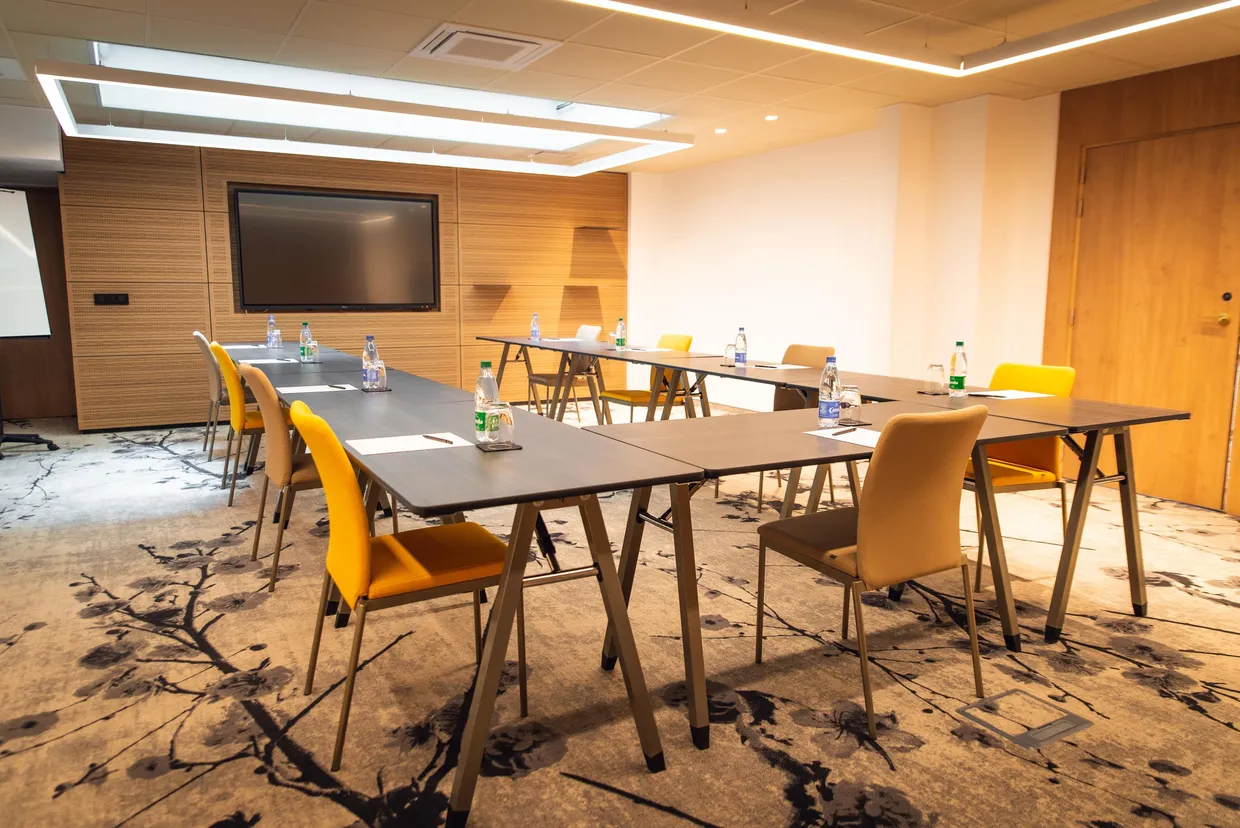 Salle de réunion avec tables et chaises disposées en U, équipée d'un écran et de bouteilles d'eau sur chaque table