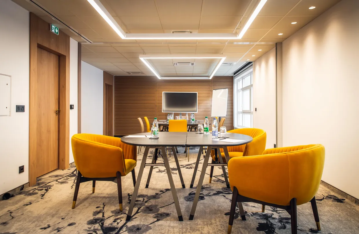 Salle de réunion avec table ronde, chaises jaunes et écran au fond