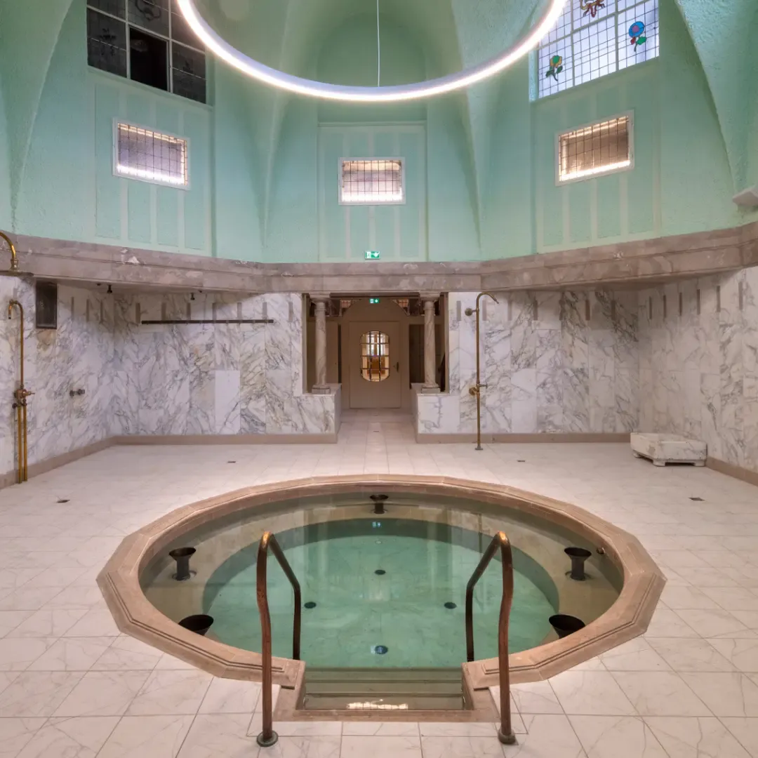 Ein kreisrunder Raum mit einem zentralen Schwimmbecken, Marmorwänden und einer hellgrünen, gewölbten Decke, die beleuchtet ist