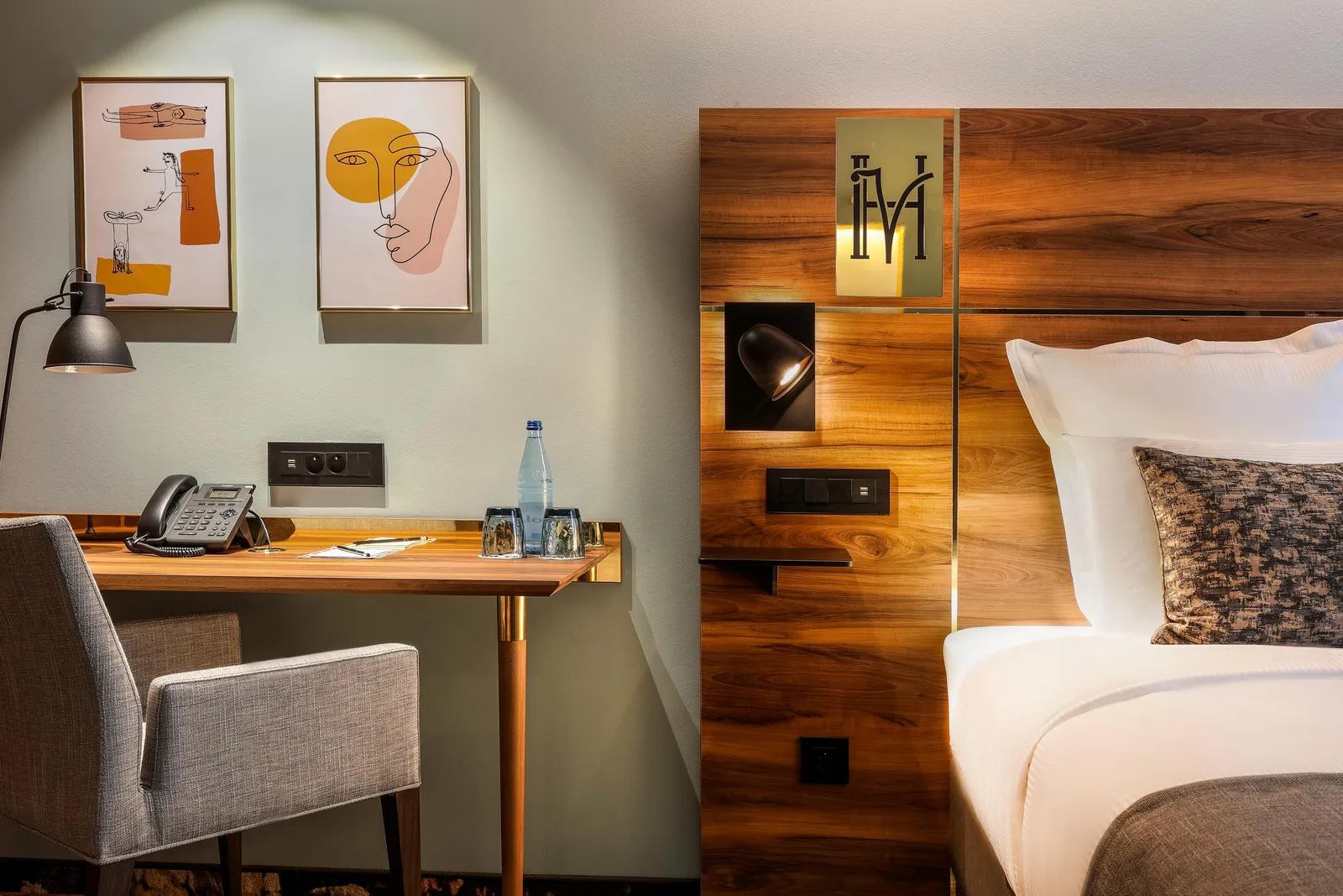 Chambre d'hôtel avec un bureau, une chaise, un téléphone, une bouteille d'eau et un lit avec des coussins