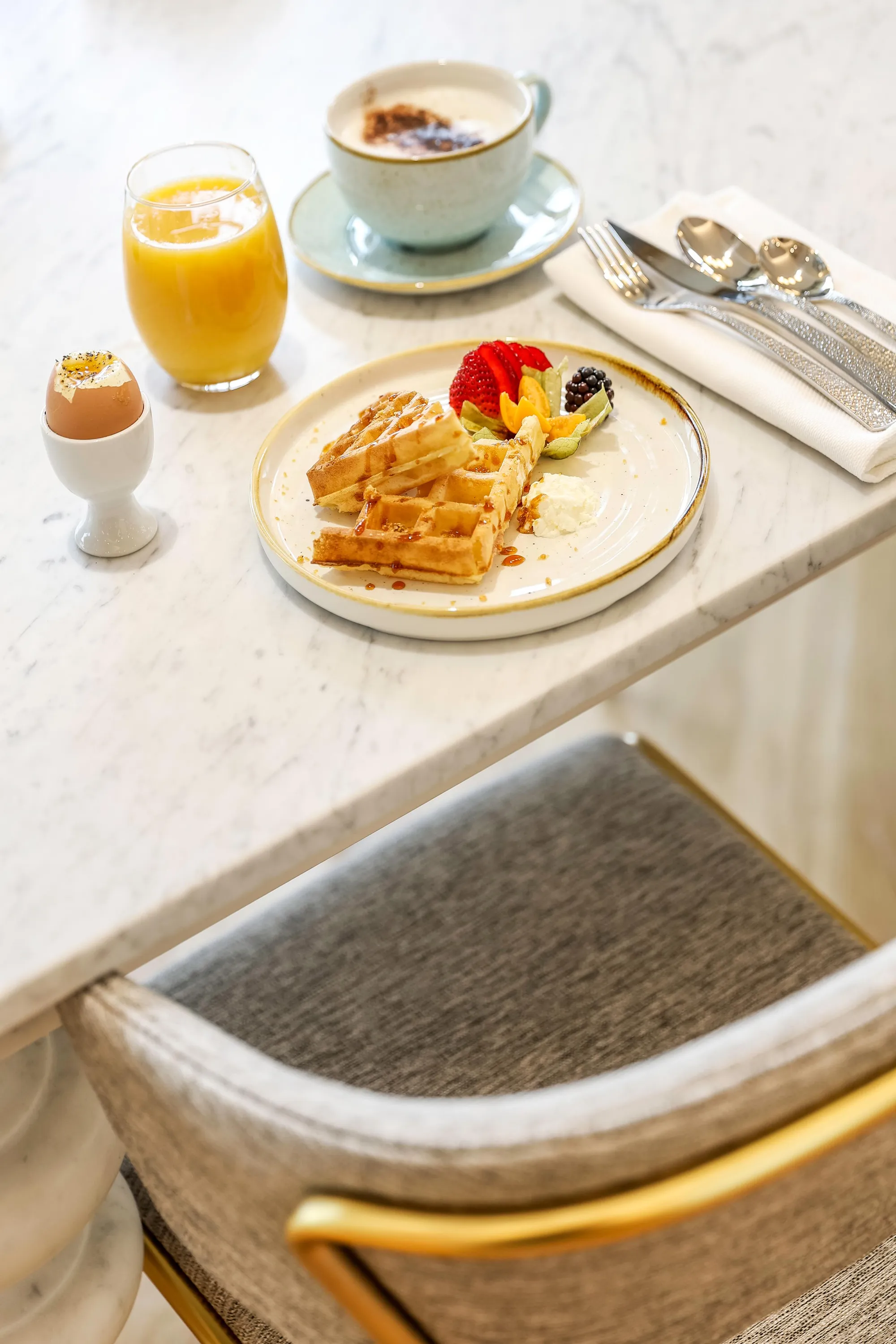 Un plateau de petit-déjeuner avec des waffles, des fruits, un œuf à la coque, un verre de jus d'orange et une tasse de café
