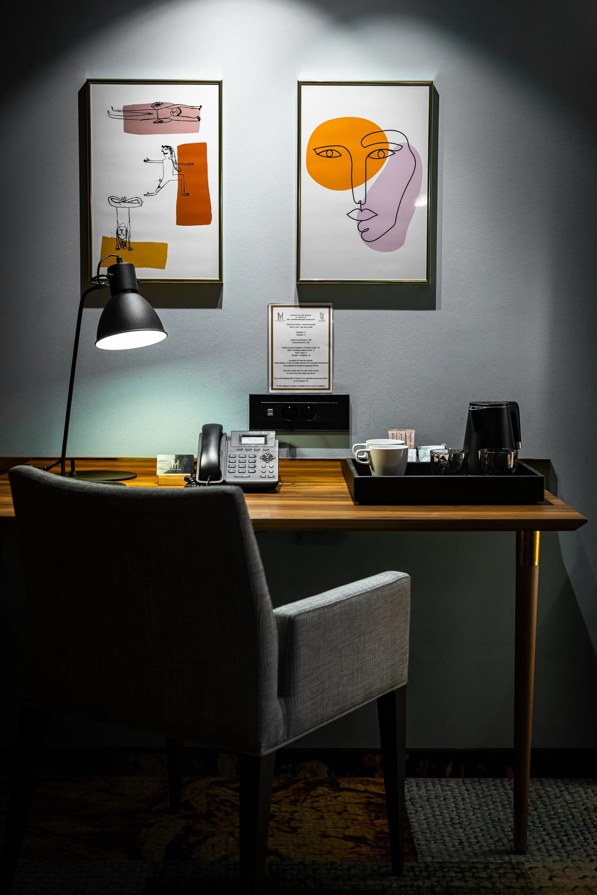 Bureau avec téléphone, lampadaire, deux chaises et deux tableaux abstraits accrochés au mur