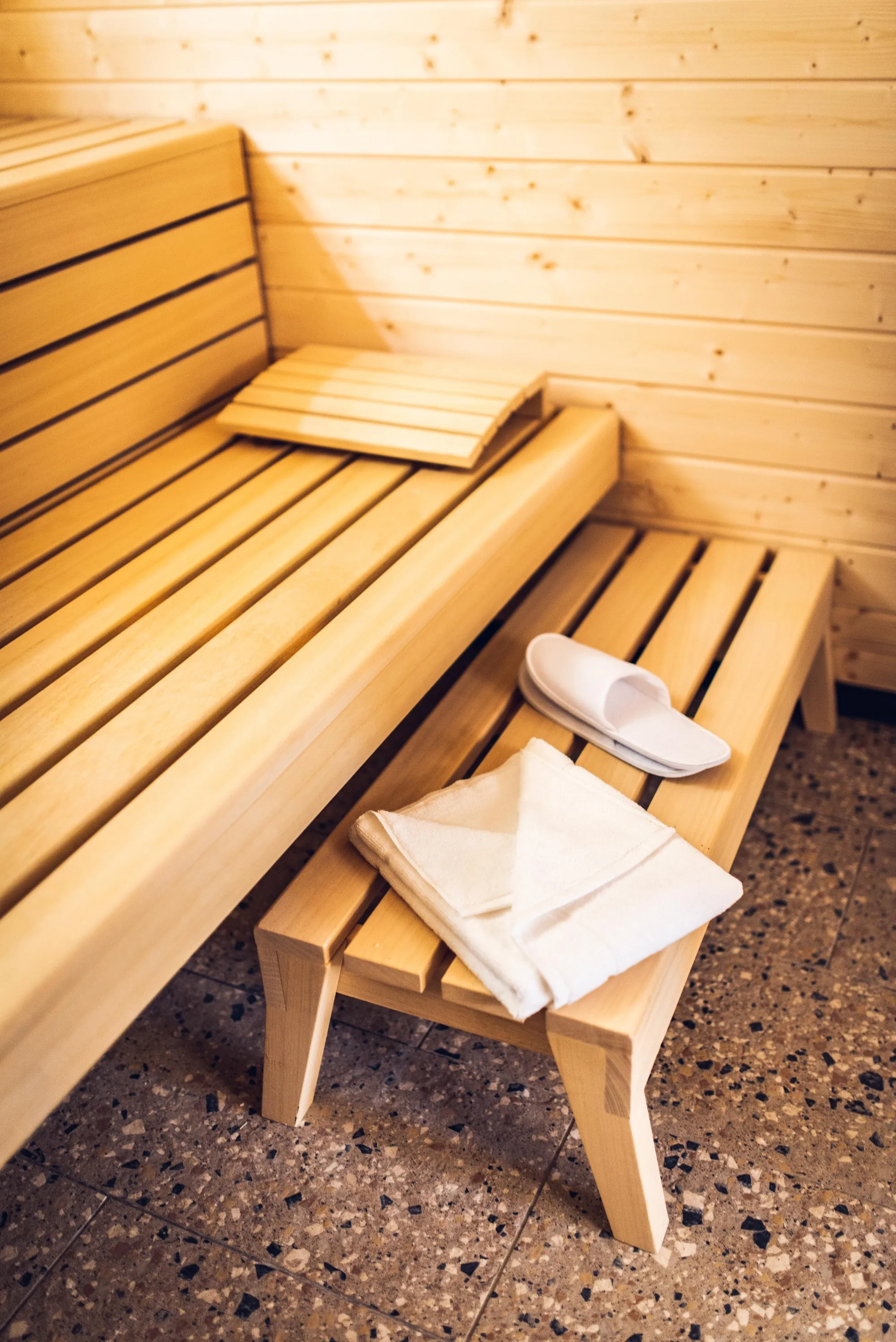 Un banc en bois clair dans un espace intérieur avec une serviette et des chaussons posés sur un tabouret devant