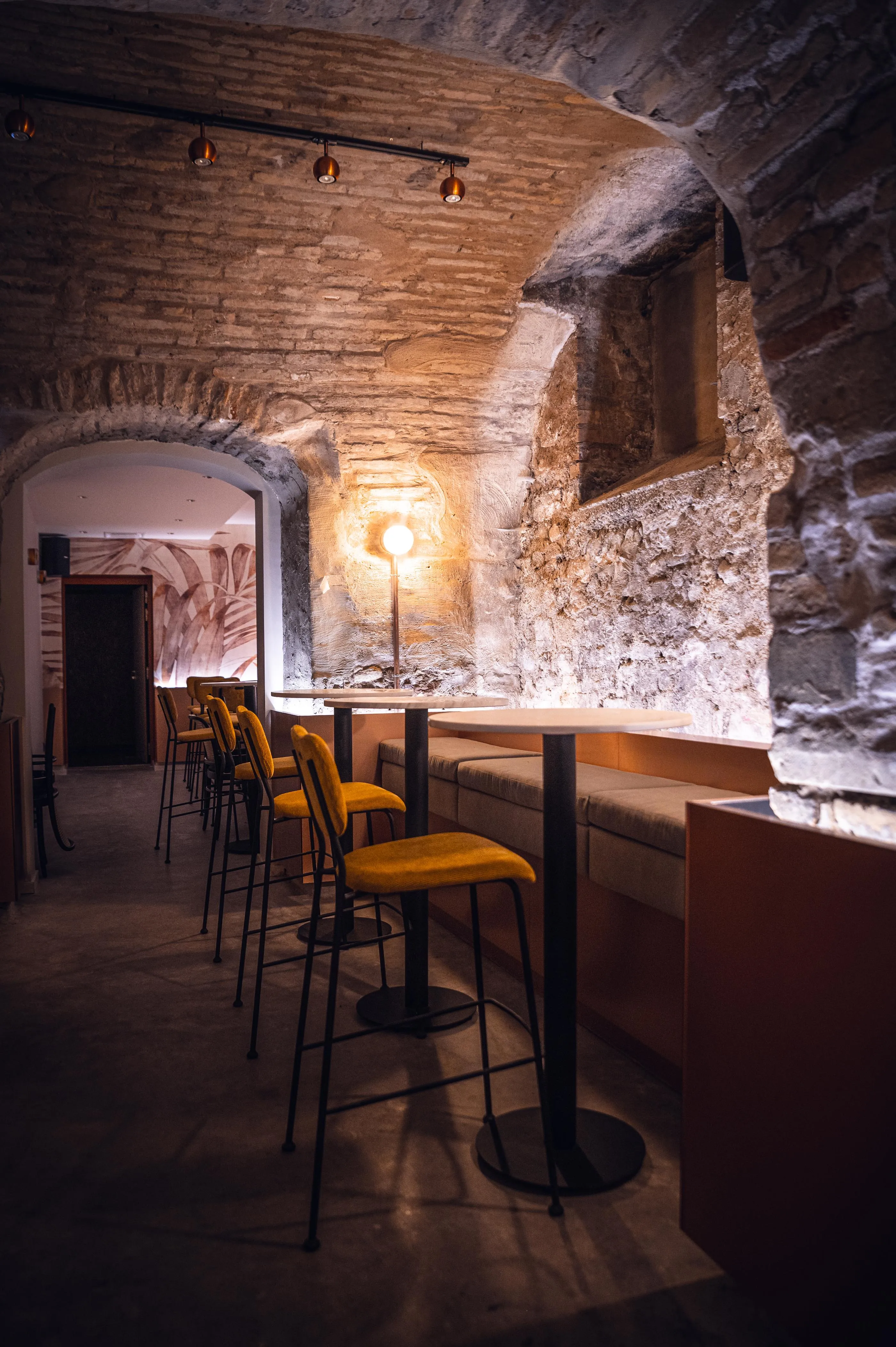 Un bar avec des tabourets jaunes et une table haute, situé dans une pièce aux murs de pierre éclairée par des lampes