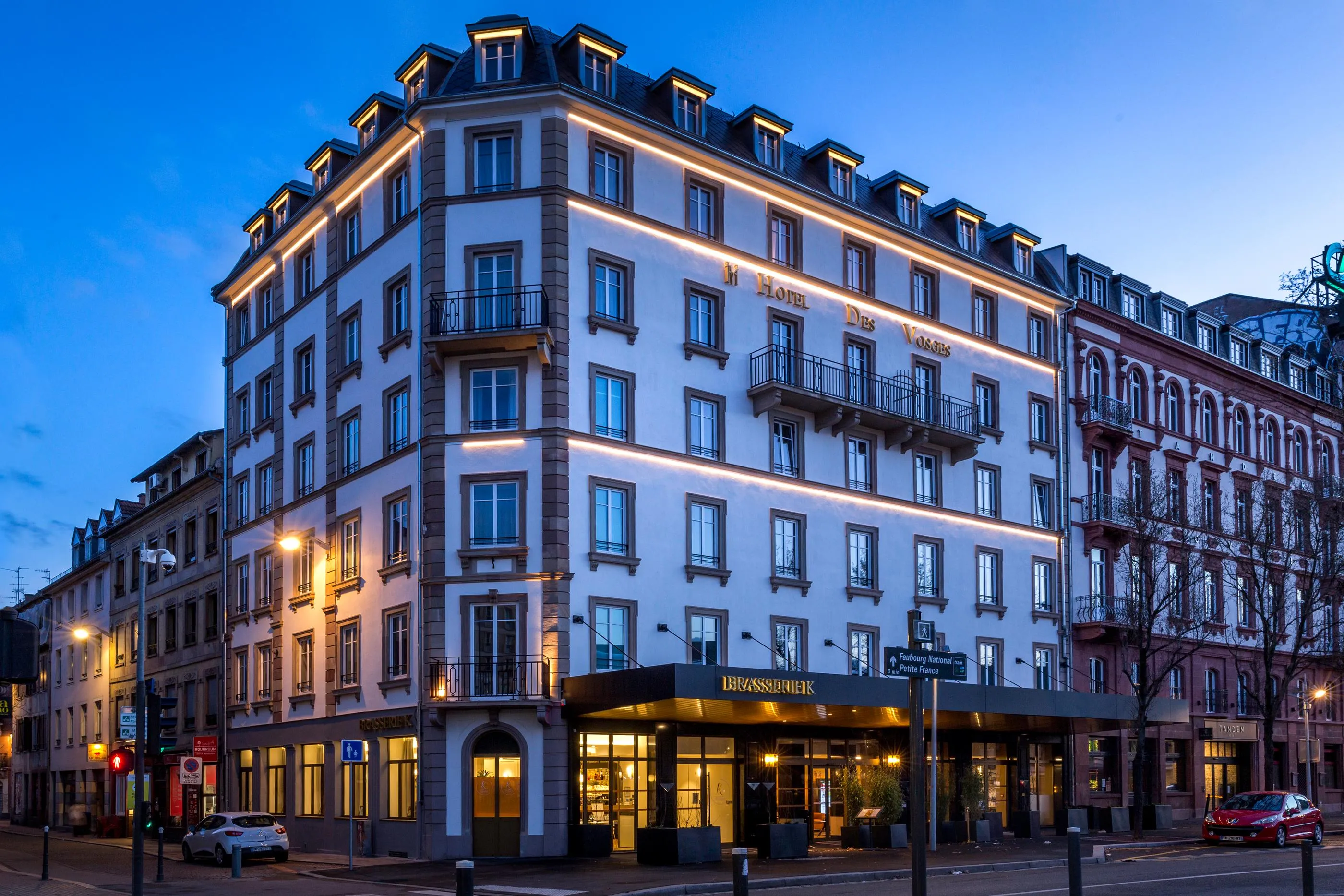 Immeuble d'angle éclairé de nuit avec l'enseigne "Hotel Des Voyageurs" et un restaurant au rez-de-chaussée