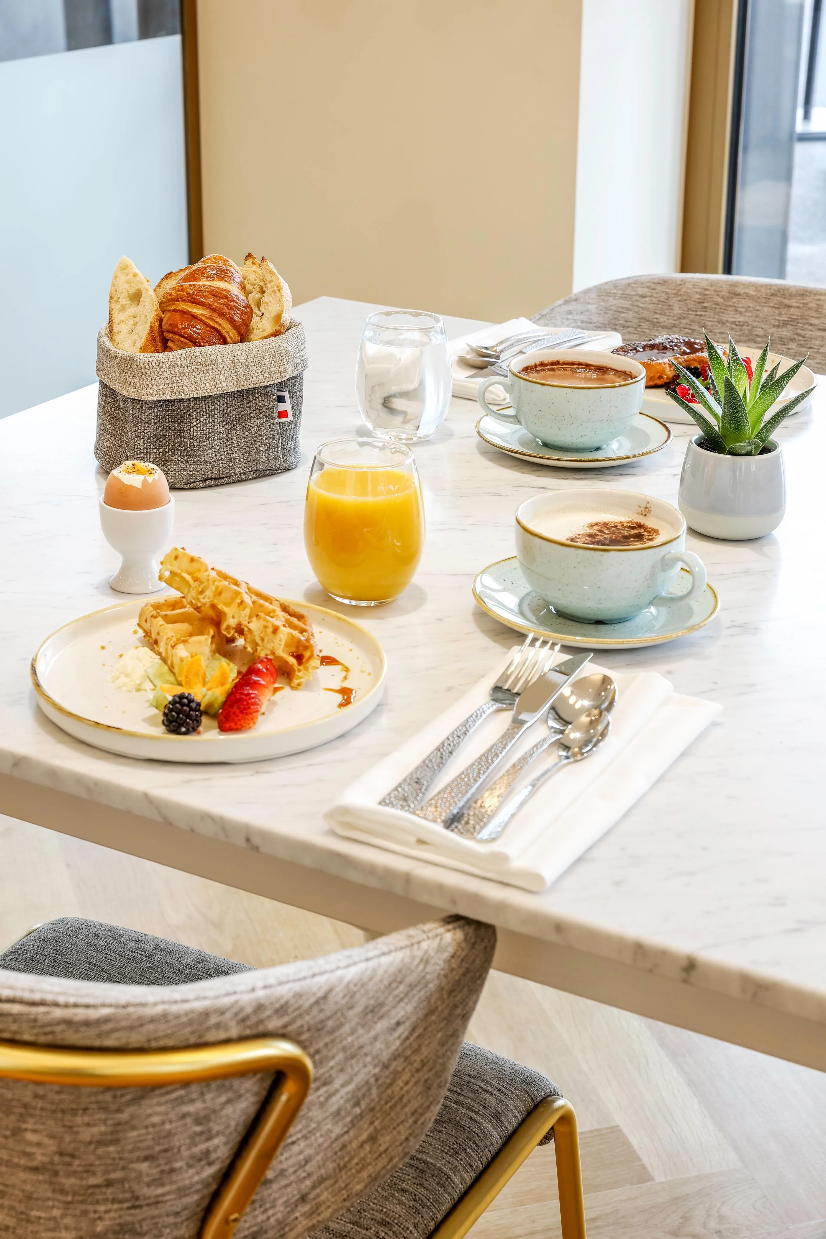 Table avec petit-déjeuner composé de croissants, œufs, waffles, jus d'orange, cafés et fruits
