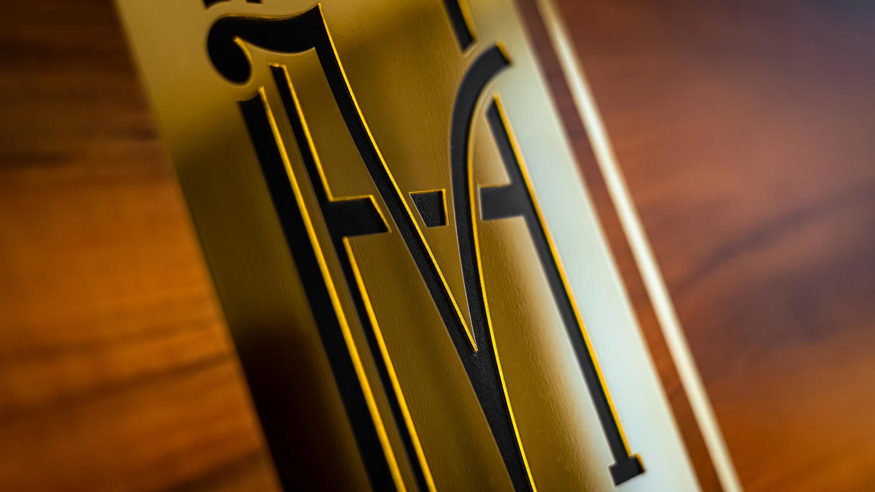 Détail d'une plaque dorée avec les lettres "MA" en relief sur fond brunâtre
