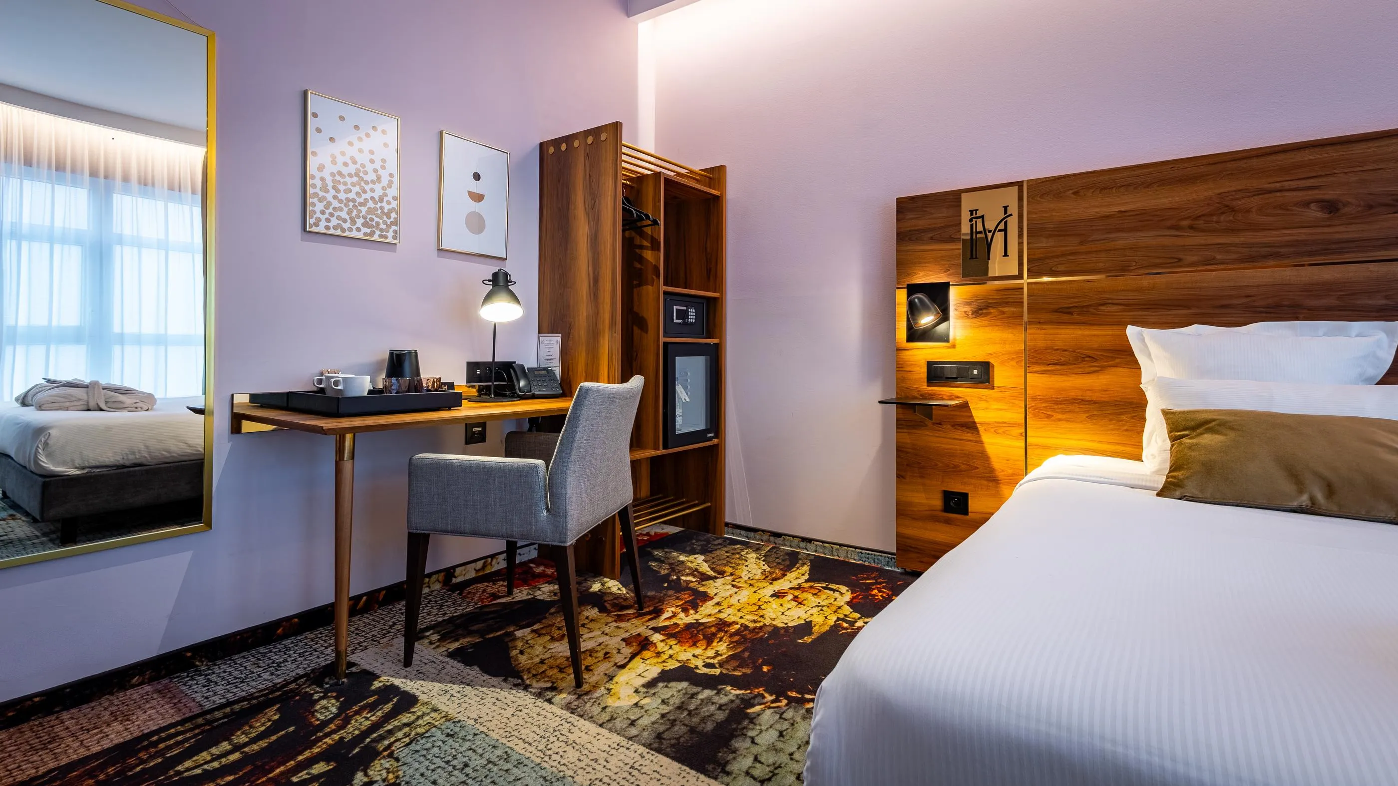 Chambre d'hôtel avec deux lits, un bureau, une chaise et un placard en bois, éclairée par une fenêtre et des lampes murales