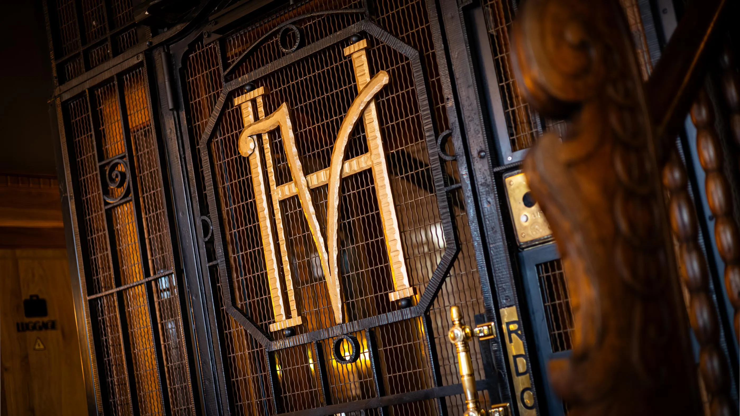 Grille métallique avec les lettres "M" et "A" en relief, éclairée par des lumières dorées, dans un cadre architectural sombre