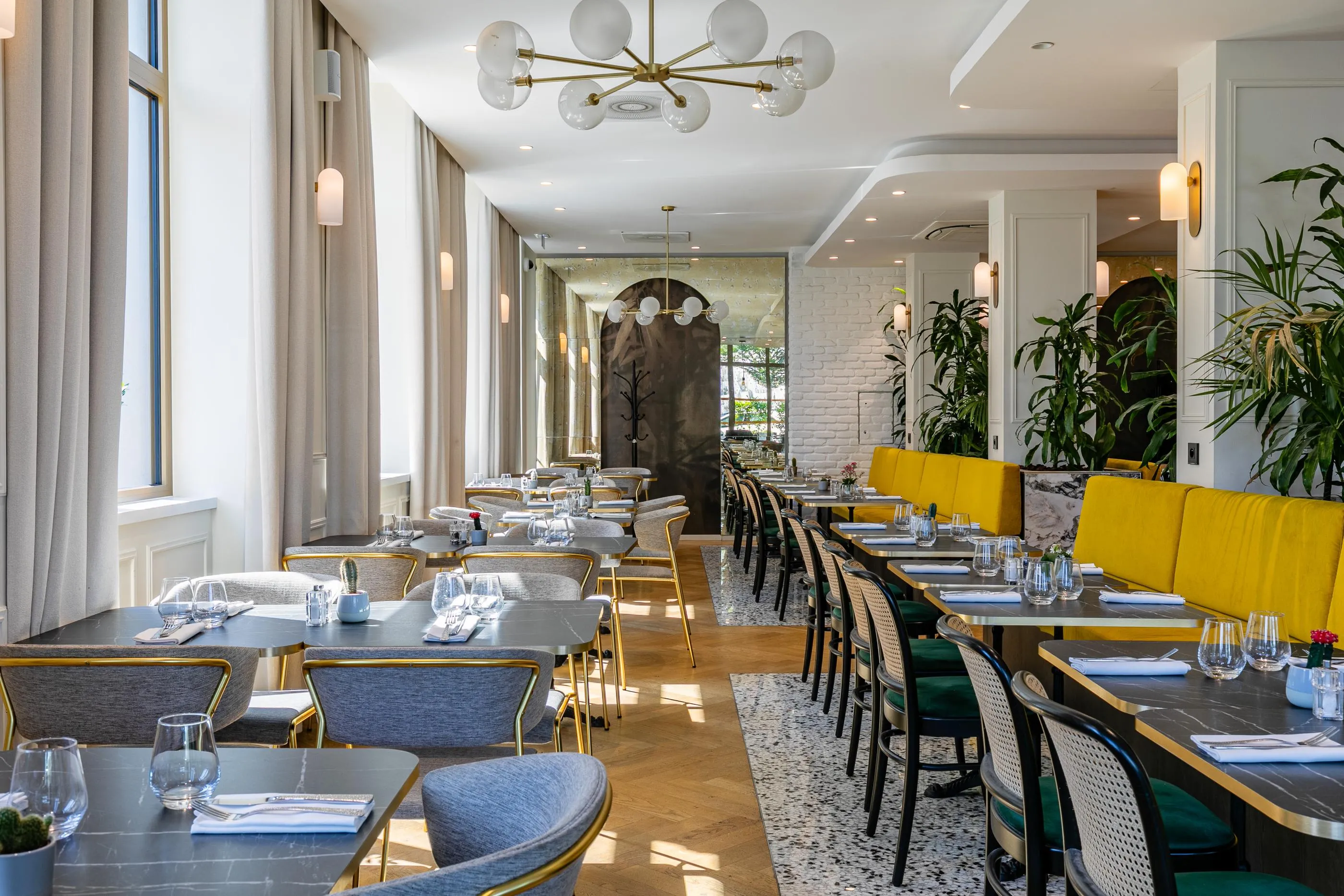 Restaurant moderne avec des tables et des chaises disposées le long d'un couloir, des plantes vertes et des luminaires suspendus