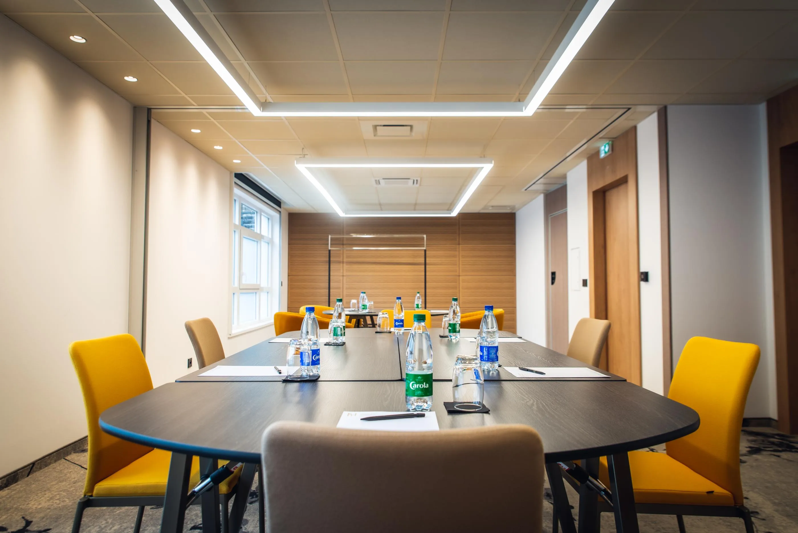 Salle de réunion avec une table rectangulaire, des chaises jaunes et des bouteilles d'eau sur la table
