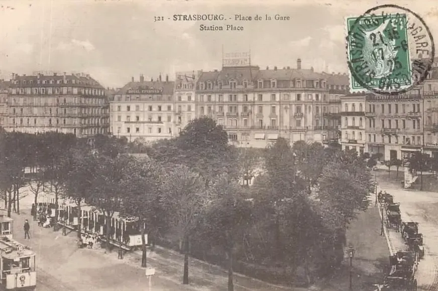 Place de la Gare à Strasbourg avec des bâtiments historiques, des arbres et des tramways en circulation