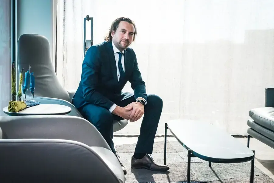 Un homme en costume bleu est assis sur un siège moderne dans un espace intérieur lumineux avec des meubles contemporains