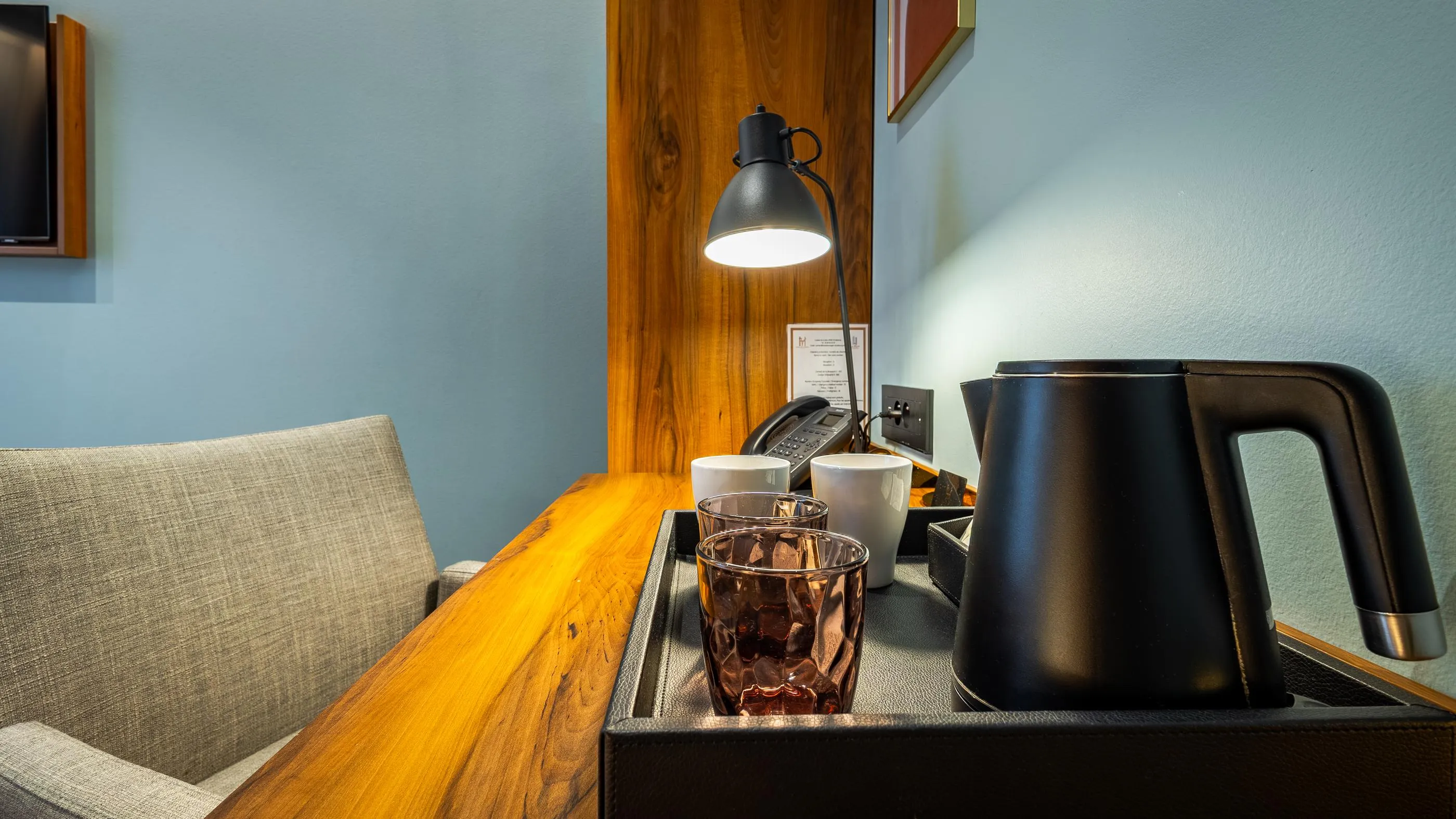 Un coin salon avec une table en bois, une lampe allumée, une bouilloire, des verres et un téléphone
