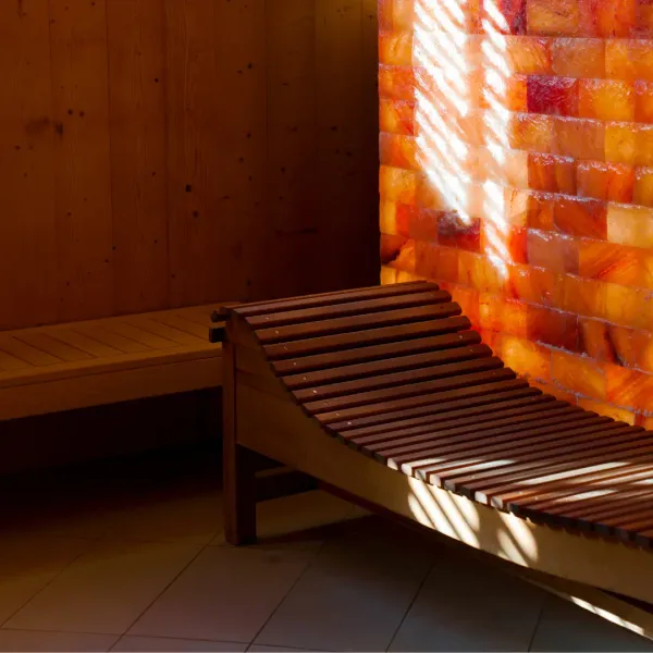 Zwei Holzbänke stehen an einer Holzwand, neben einer von Sonnenlicht beleuchteten orangen Steinwand.