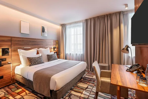 Chambre d'hôtel avec un lit double, une table de travail, une fenêtre avec des rideaux et un fauteuil