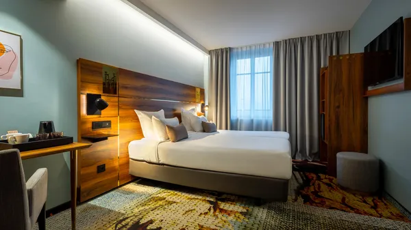 Hotel room with a double bed, a work desk, curtains, and wall decor