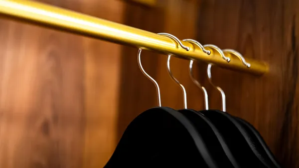Des cintres métalliques accrochés à une tringle dorée dans un placard en bois