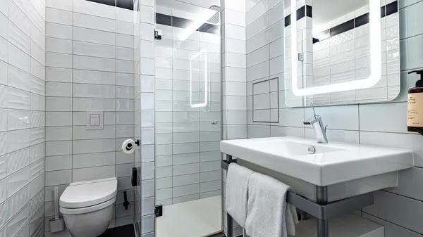 Salle de bain moderne avec toilettes, lavabo, miroir éclairé et douche aux carreaux blancs