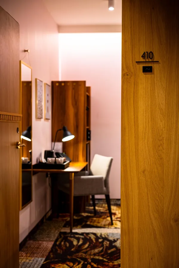 Vue d'une chambre d'hôtel avec un bureau, une lampe et une chaise, vue depuis le couloir avec la porte numérotée 410 ouverte