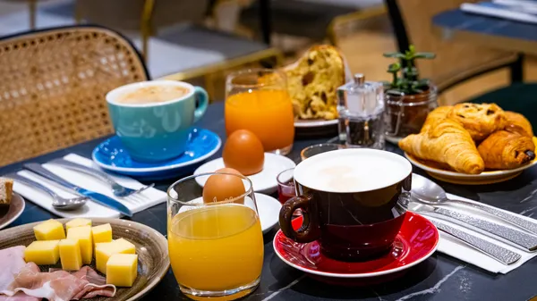 Frühstückstisch mit Kaffee, Orangensaft, Croissants, Eiern, Butter, Aufschnitt und Besteck