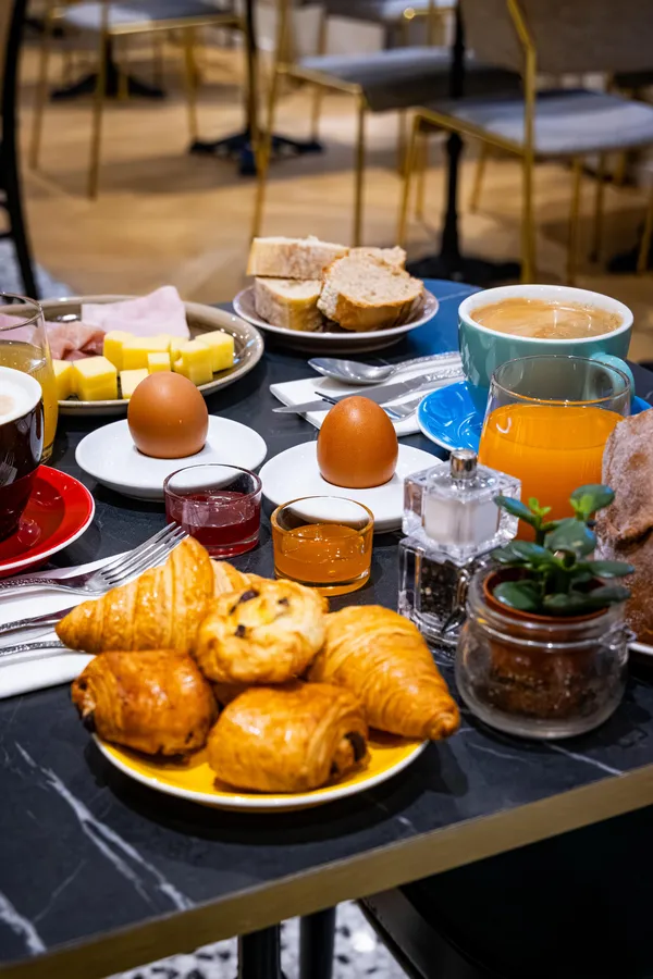 Table garnie de croissants, œufs, pain, jus d'orange, café et autres aliments pour un petit-déjeuner