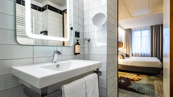 Modern bathroom with white sink, illuminated mirror, and open door leading to a bedroom