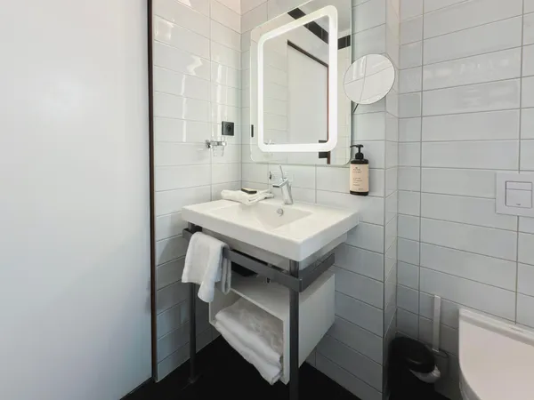 Un lavabo blanc sur pied noir avec un miroir rectangulaire éclairé, des serviettes et un flacon de produit posés à côté