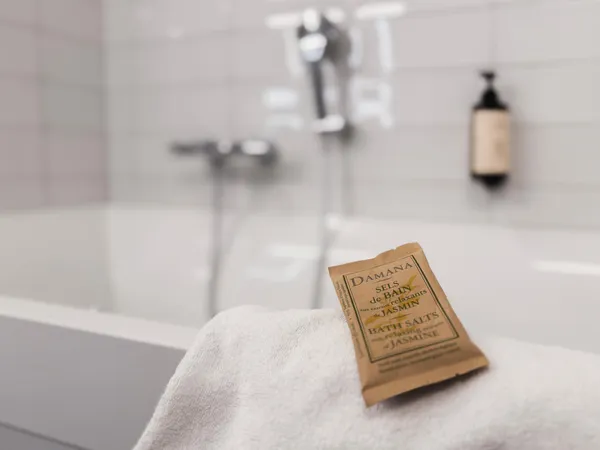 Un sachet de sels de bain au jasmin repose sur une serviette blanche près d'une baignoire